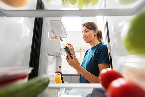 healthy eating and diet concept - woman at fridge with smartphone making list of necessary food at home kitchen