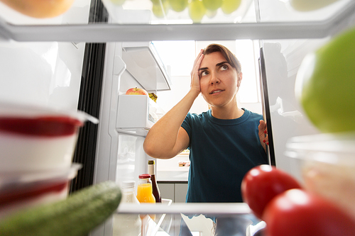 healthy eating, food and diet concept - crazy woman at open fridge holding to head