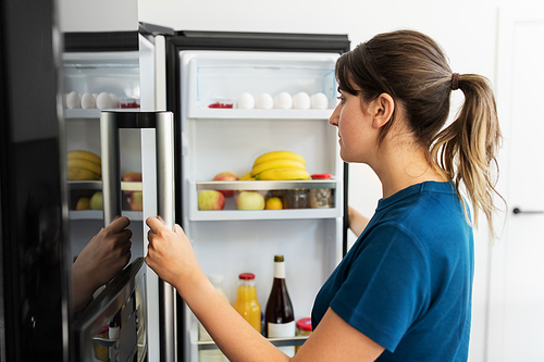 healthy eating, food and diet concept - woman at open fridge at home kitchen
