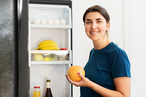 healthy eating, food and diet concept - happy woman taking grapefruit from fridge at home kitchen