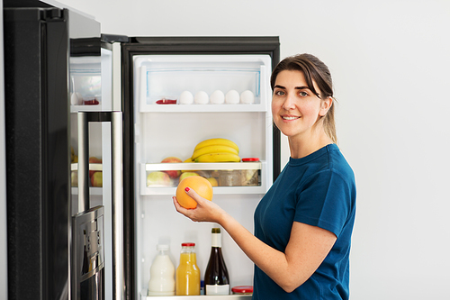 healthy eating, food and diet concept - happy woman taking grapefruit from fridge at home kitchen