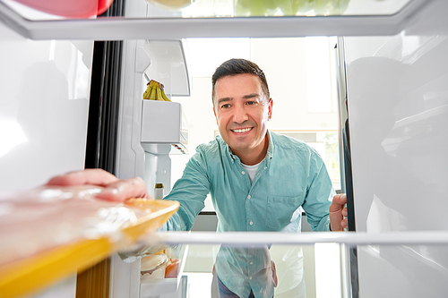 food, eating and diet concept - smiling middle-aged man taking meat from fridge at kitchen