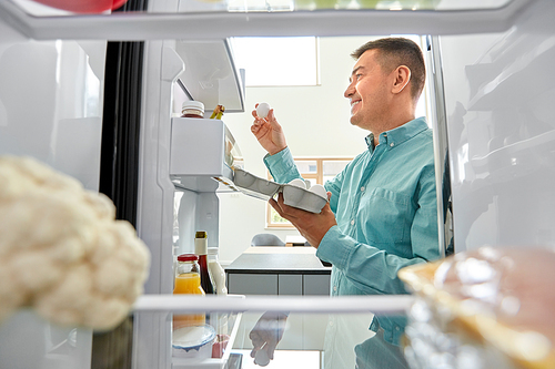 food, eating and diet concept - smiling middle-aged man taking eggs from fridge at kitchen