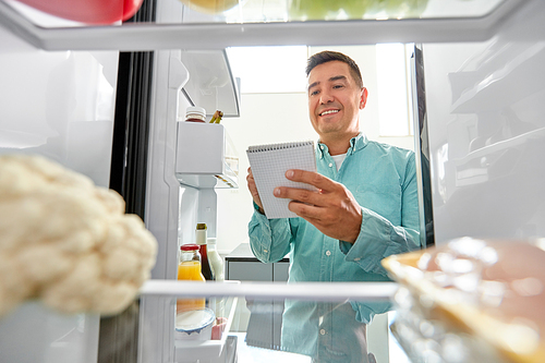 healthy eating and diet concept - smiling middle-aged man opening fridge and making list of necessary food at home kitchen
