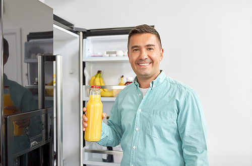 healthy eating, food and diet concept - middle-aged man taking bottle of orange juice from fridge at home kitchen