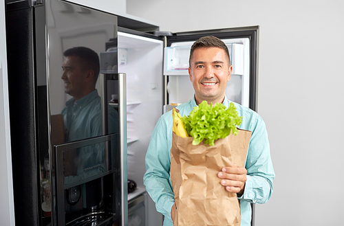 eating, diet and storage concept - smiling middle-aged man with new purchased food in paper bag at home fridge