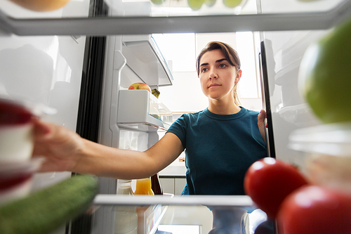 healthy eating, food and diet concept - woman taking yoghurt from fridge at home kitchen
