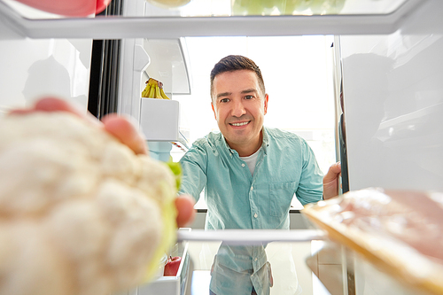 healthy eating, food and vegetable diet concept - happy middle-aged man taking cauliflower from fridge at home kitchen