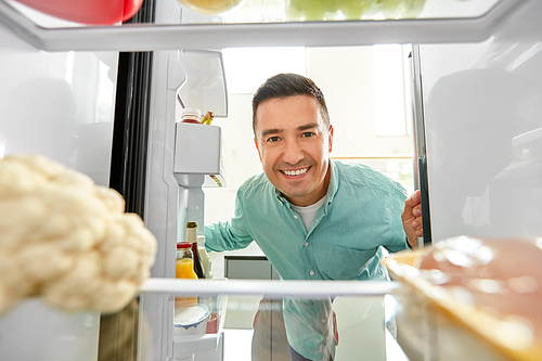 eating and diet concept - smiling middle-aged man looking for food in fridge at kitchen
