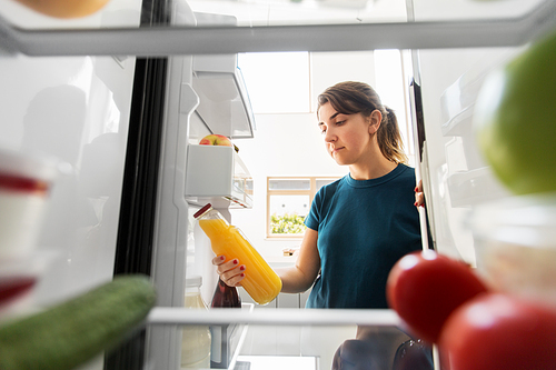 healthy eating, food and diet concept - woman taking bottle of orange juice from fridge at home kitchen