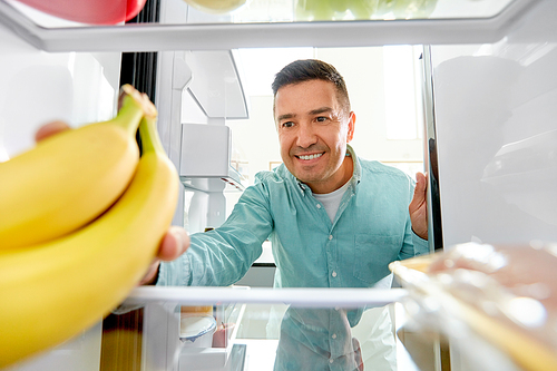 healthy eating, food and diet concept - happy middle-aged man taking banana from fridge at home kitchen