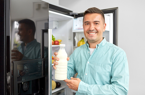 healthy eating, food and  concept - middle-aged man taking bottle of milk from fridge at home kitchen