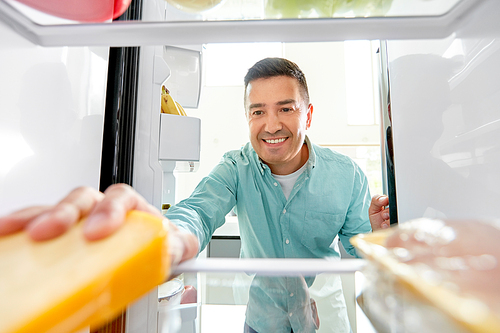 food, eating and diet concept - smiling middle-aged man taking cheese from fridge at kitchen