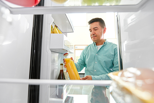 healthy eating, food and diet concept - middle-aged man taking bottle of orange juice from fridge at home kitchen