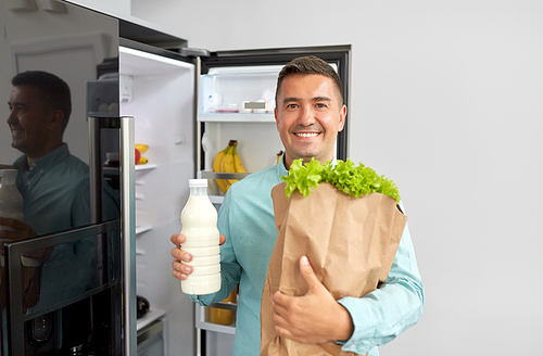 eating,  and storage concept - smiling middle-aged man with new purchased food in paper bag at home fridge