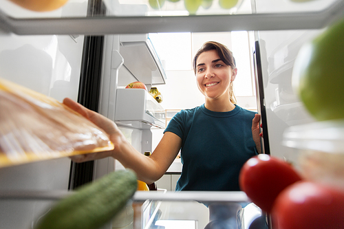 healthy eating, food and diet concept - happy woman taking meat from fridge at home kitchen