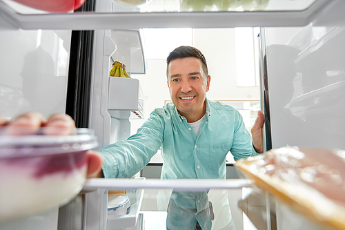 food, eating and diet concept - smiling middle-aged man taking yoghurt from fridge at kitchen