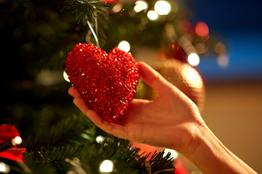 holidays, celebration and people concept - woman hands decorating christmas tree with red heart