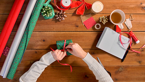 holidays, new year and christmas concept - hands packing gift box and tying ribbon on wooden table