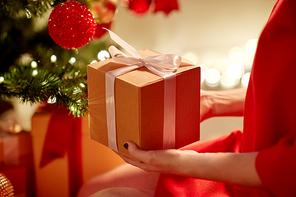 winter holidays, celebration and people concept - close up of woman with gift box at christmas tree at home