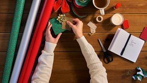 holidays, new year and christmas concept - hands packing gift box and attaching tag to it on wooden table
