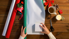 holidays, new year and christmas concept - hands wrapping gift box into green paper on wooden table