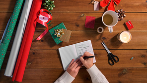 holidays, new year and christmas concept - female's hands writing to do list in notebook on wooden table