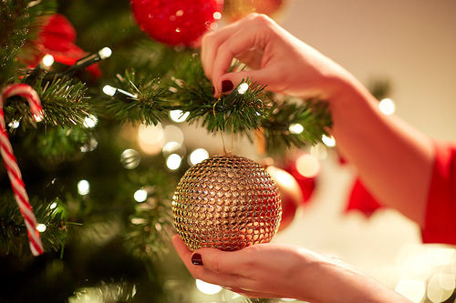 holidays, celebration and people concept - woman hands decorating christmas tree with ball