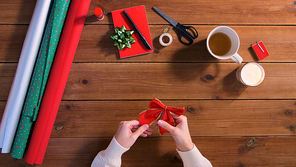 holidays, new year and christmas concept - hands with bow setting stuff for gifts wrapping on wooden table