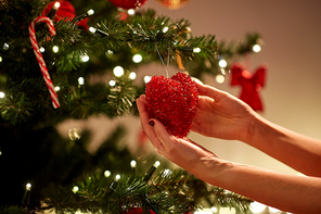 holidays, celebration and people concept - woman hands decorating christmas tree with red heart