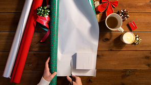 holidays, new year and christmas concept - hands wrapping gift box into green paper on wooden table