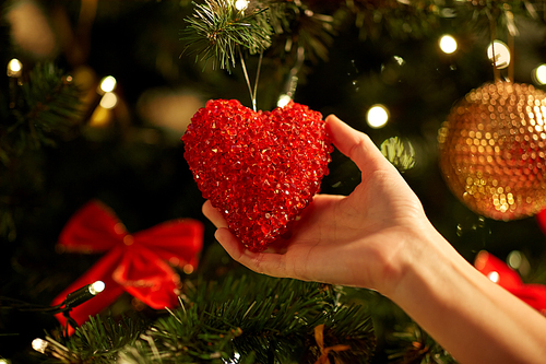holidays, celebration and people concept - woman hands decorating christmas tree with red heart