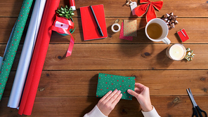 holidays, new year and christmas concept - hands wrapping gift box into green paper on wooden table