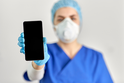 medicine, health and pandemic concept - close up of young female doctor or nurse wearing face protective mask or respirator for protection from virus disease with smartphone