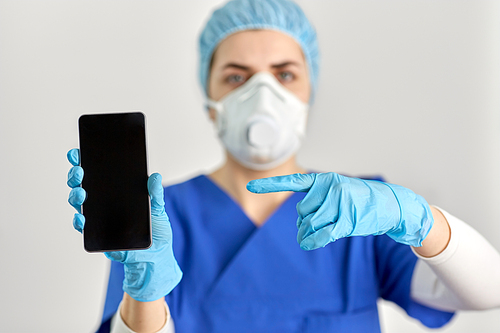 medicine, health and pandemic concept - close up of young female doctor or nurse wearing face protective mask or respirator for protection from virus disease with smartphone