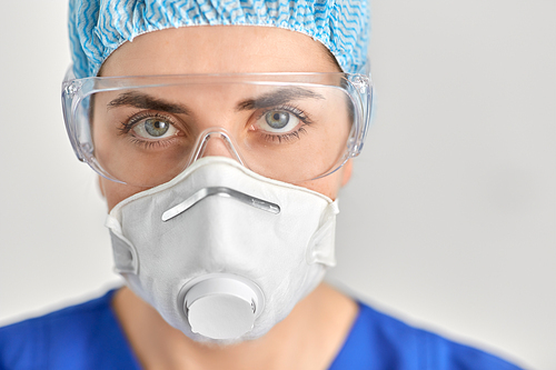 medicine, healthcare and pandemic concept - close up of young female doctor or nurse wearing goggles and face protective mask or respirator for protection from virus disease