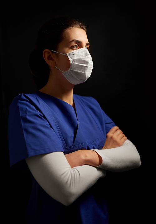 health, medicine and pandemic concept - young female doctor or nurse wearing face protective mask for protection from virus disease over black background