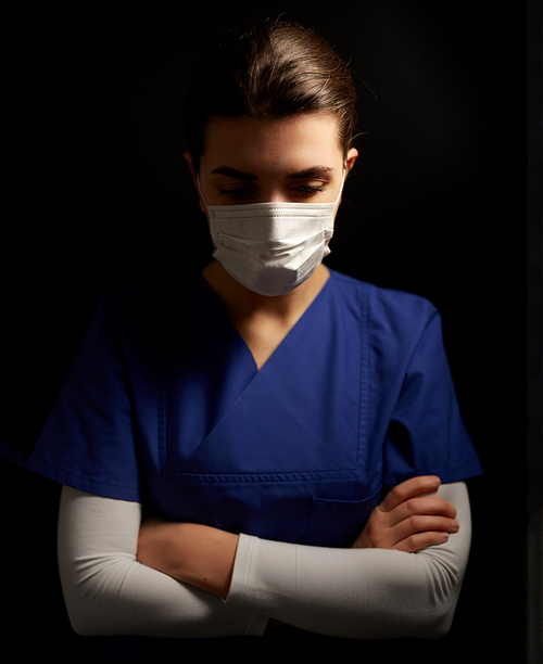 health, medicine and pandemic concept - sad young female doctor or nurse wearing face protective mask for protection from virus disease over black background