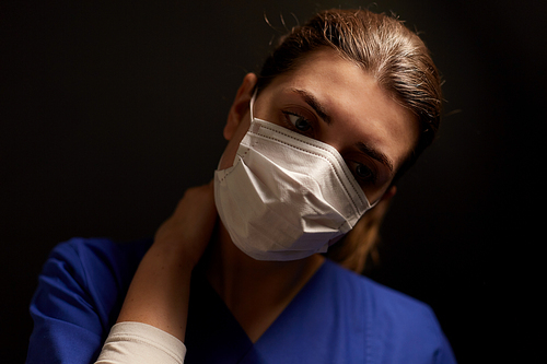 health, medicine and pandemic concept - tired young female doctor or nurse wearing face protective mask for protection from virus disease over black background