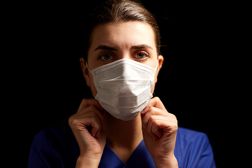 health, medicine and pandemic concept - young female doctor or nurse wearing face protective mask for protection from virus disease over black background