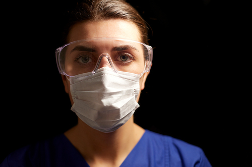 health, medicine and pandemic concept - young female doctor or nurse wearing goggles and face protective mask for protection from virus disease over black background