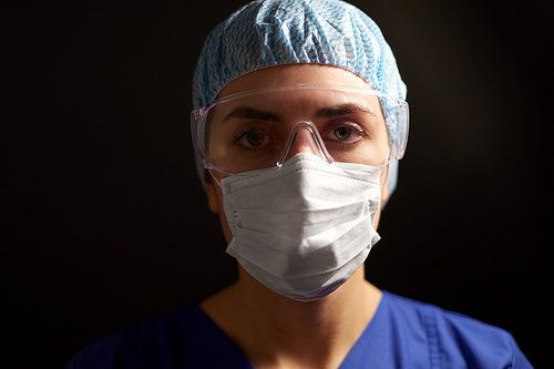 health, medicine and pandemic concept - close up of young female doctor or nurse wearing goggles, hat and face protective mask for protection from virus disease over black background