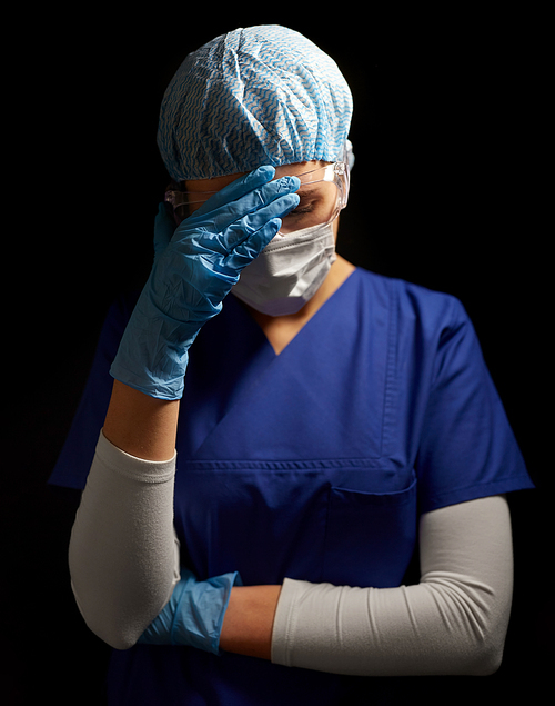 health, medicine and pandemic concept - sad young female doctor or nurse wearing goggles, hat and face protective mask for protection from virus disease over black background