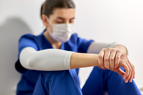 medicine, healthcare and pandemic concept - sad young female doctor or nurse wearing face protective mask for protection from virus disease sitting on floor at hospital