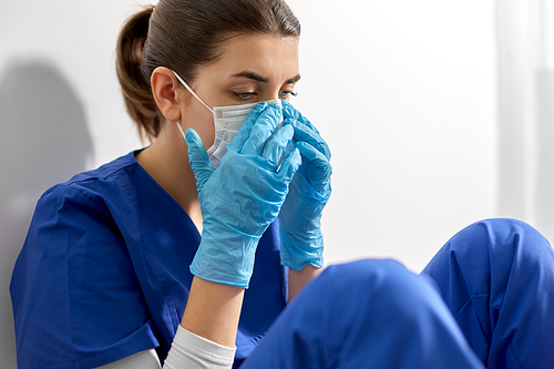 medicine, healthcare and pandemic concept - sad young female doctor or nurse wearing face protective mask for protection from virus disease sitting on floor at hospital