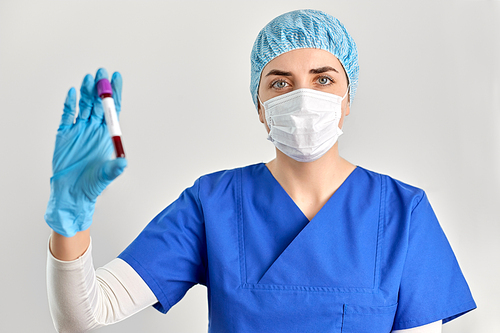 medicine, health and pandemic concept - young female doctor or nurse wearing face protective medical mask for protection from virus disease holding beaker with blood test