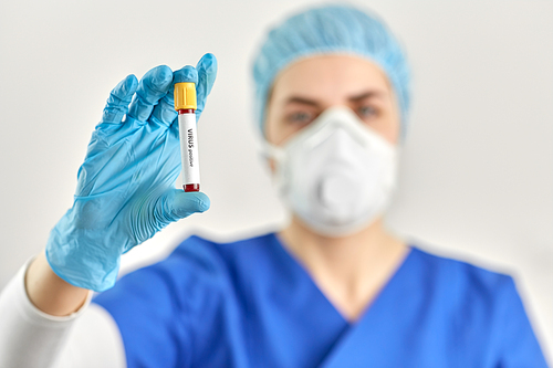 medicine, health and pandemic concept - close up of young female doctor or nurse holding beaker with virus positive blood test