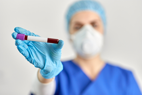 medicine, health and pandemic concept - close up of young female doctor or nurse holding beaker with blood test