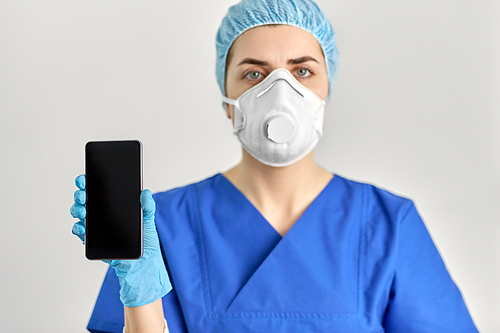 medicine, health and pandemic concept - close up of young female doctor or nurse wearing face protective mask or respirator for protection from virus disease with smartphone