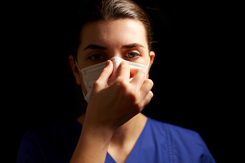 health, medicine and pandemic concept - young female doctor or nurse adjusting face protective mask for protection from virus disease over black background